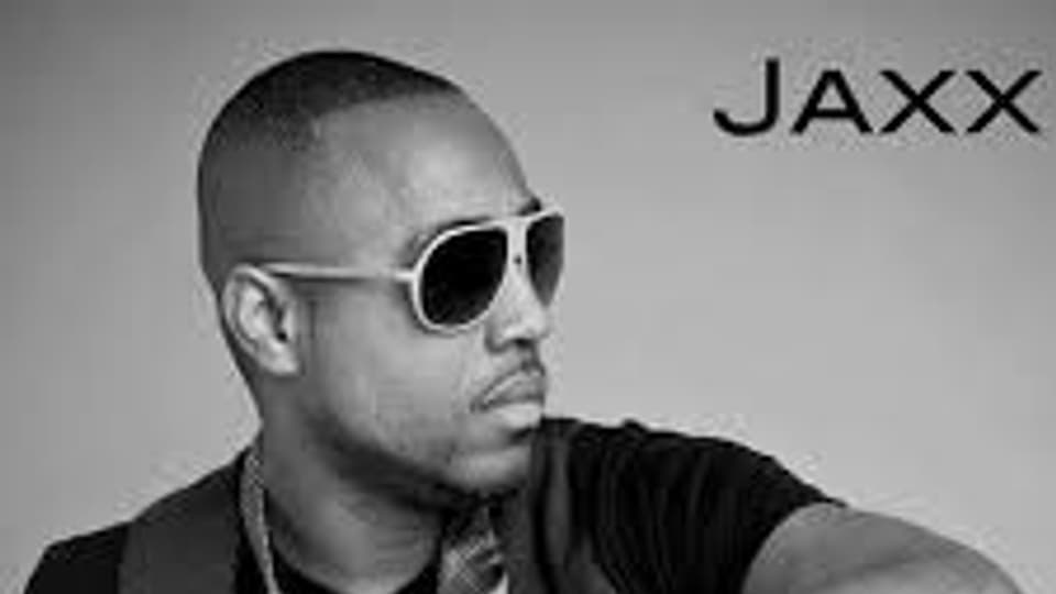 Black-and-white portrait of JAXX wearing sunglasses and sitting sideways