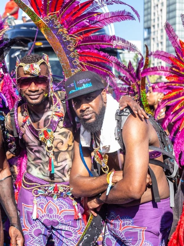 Four masqueraders in purple and blue beaded costumes with feathered headpieces posing together