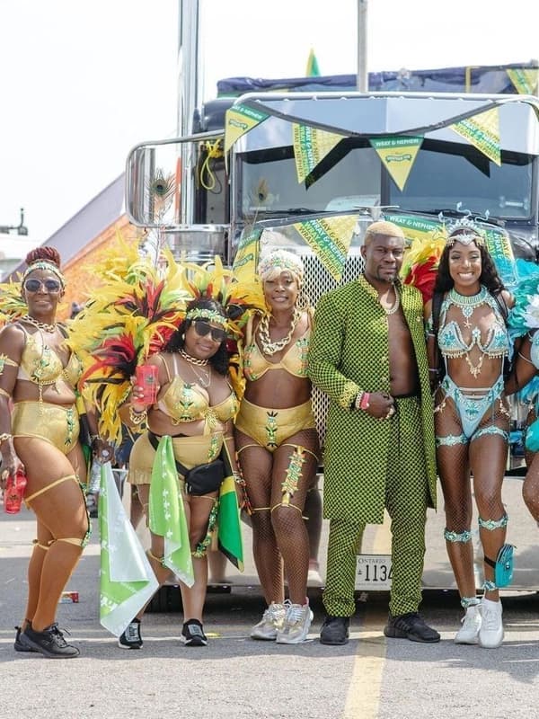 A group of masqueraders in yellow, green and black costumes in front of a parade truck