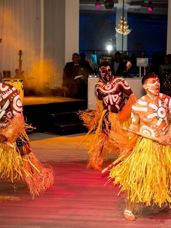 Performers in painted bodies and straw skirts walking a runway at an indoor event