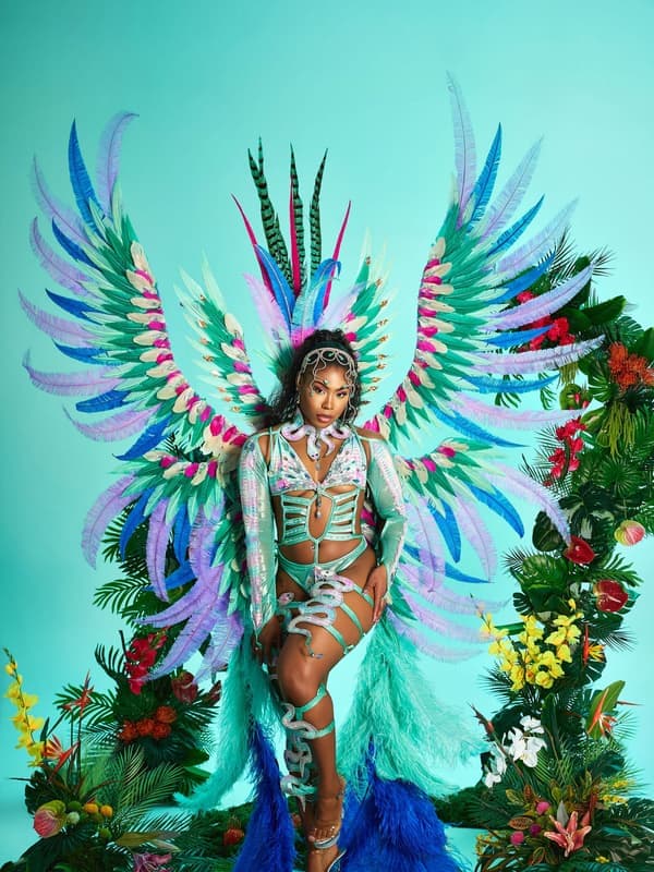Model in a teal and white costume with feathered wings and flowers on a turquoise set