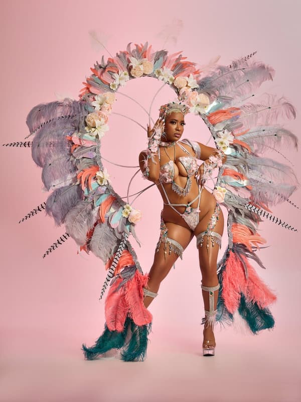 Model in a pale pink costume with a ring of feathers and flowers on a pink set