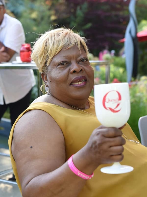 A smiling woman in a yellow top holding a wine glass at an outdoor event