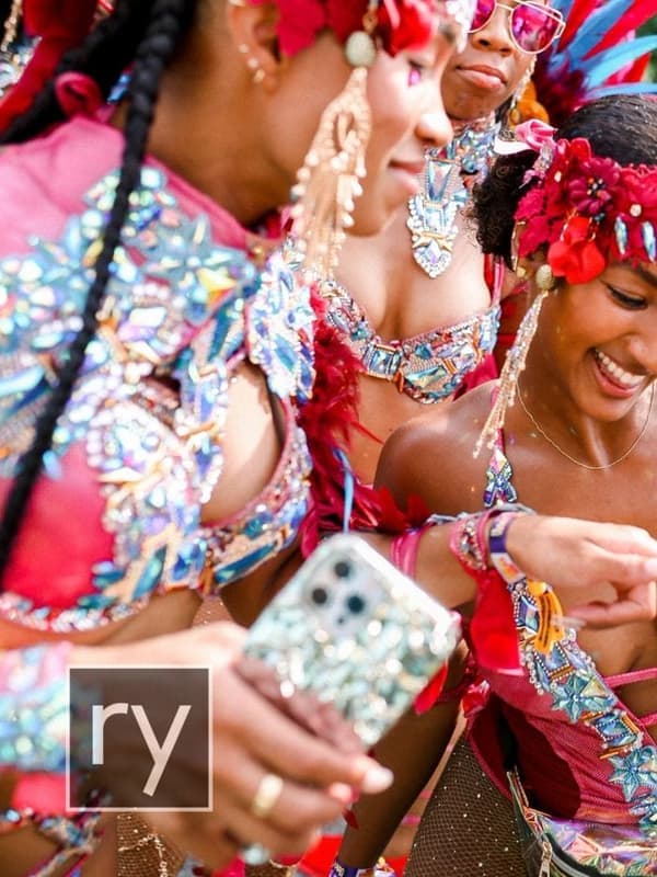 Masqueraders in red and white costumes laughing together on the road, with the Tribal Carnival logo