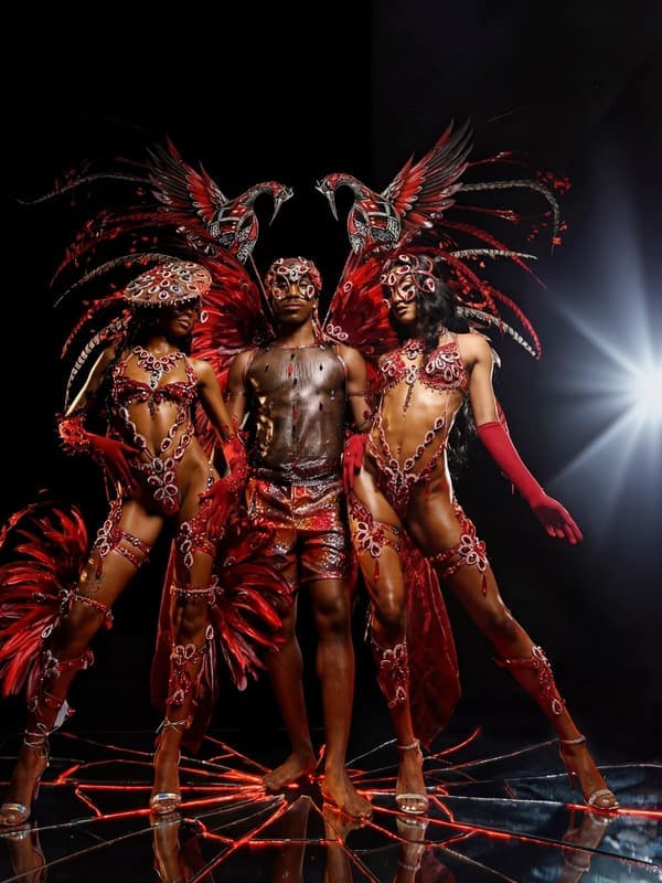 Three performers in dark red feathered costumes under stage lights