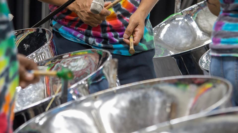 Close-up of steelpan players in colourful clothes with mallets over silver pans