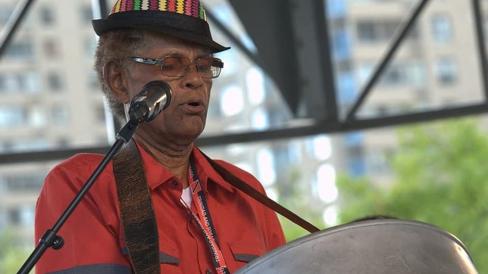 Panman Pat in a colourful hat playing steelpan on a stage